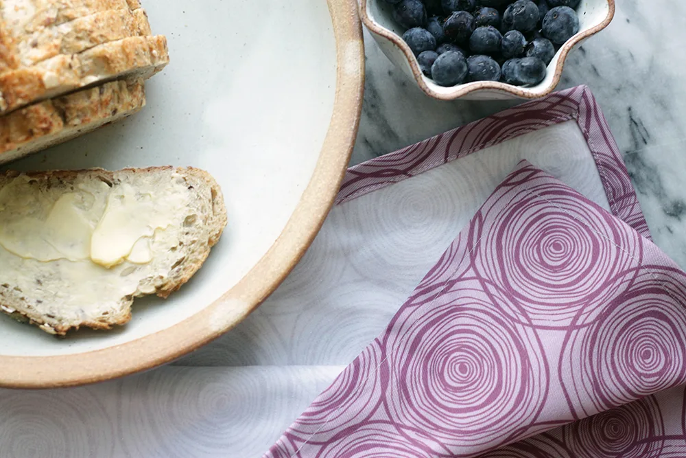 plate with bread and butter, bowl of blueberries and a napkin with a purple onion design on it, all sitting on a marble table