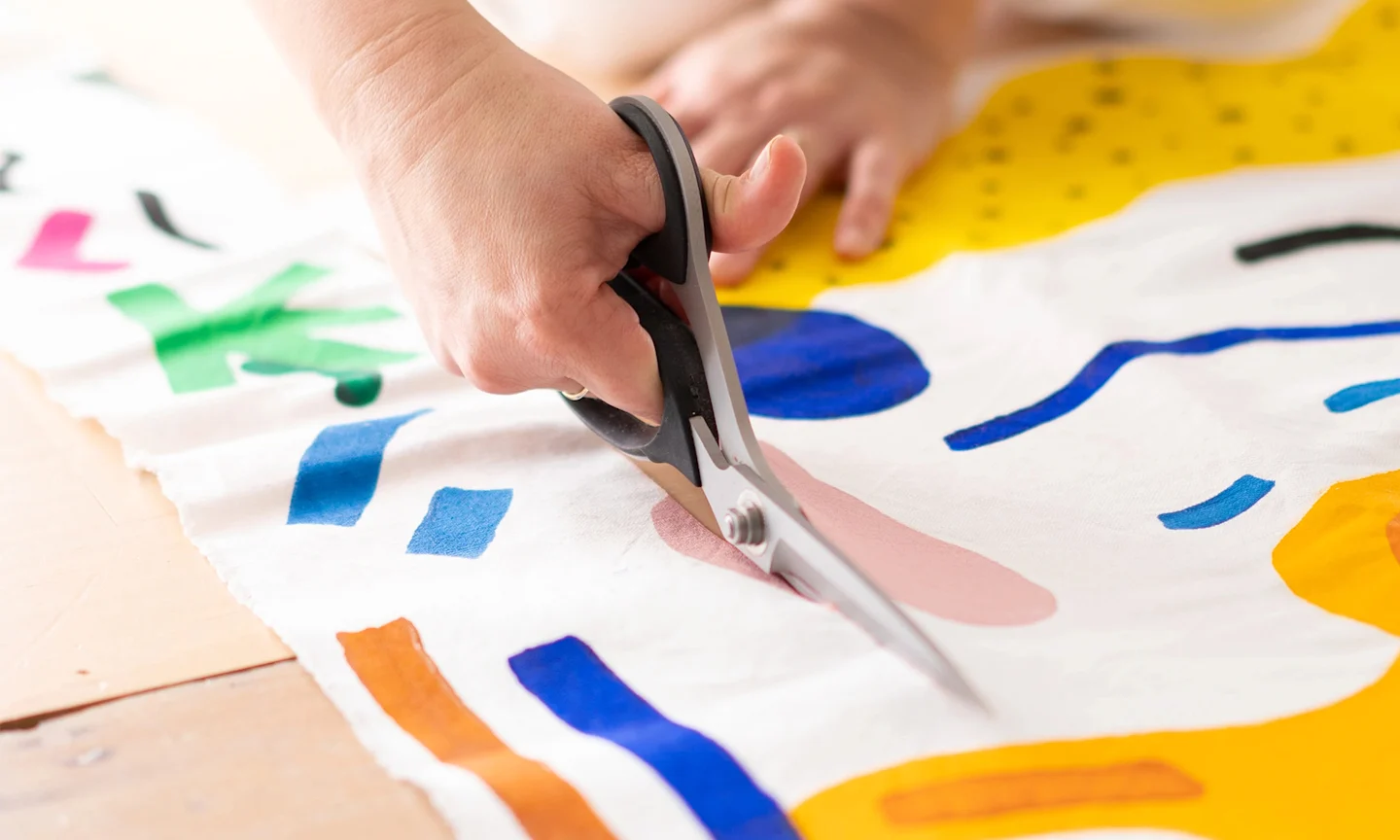 Hands using shears to cut colorful abstract fabric.