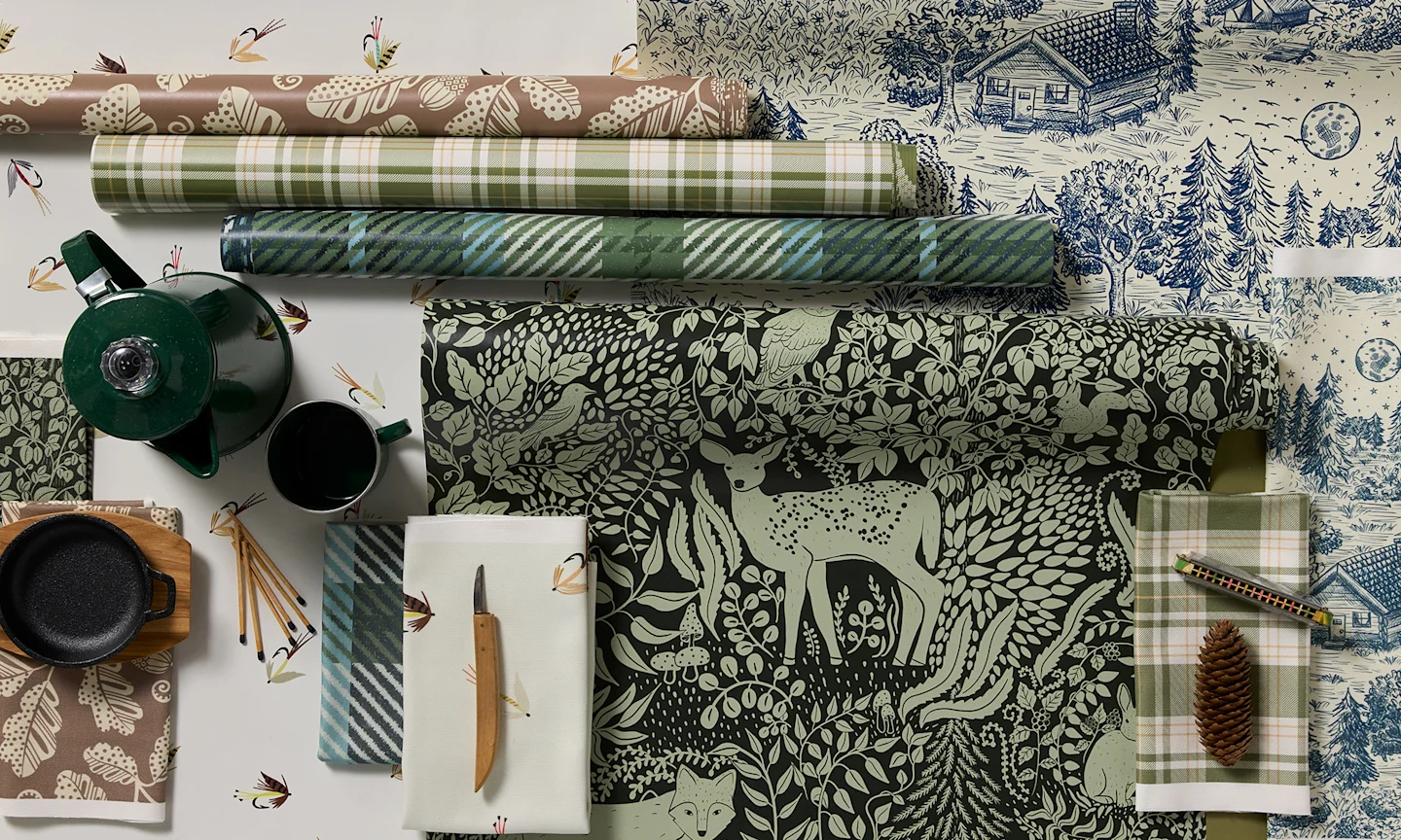 Cabincore wallpaper rolls and fabric swatches on a green background.