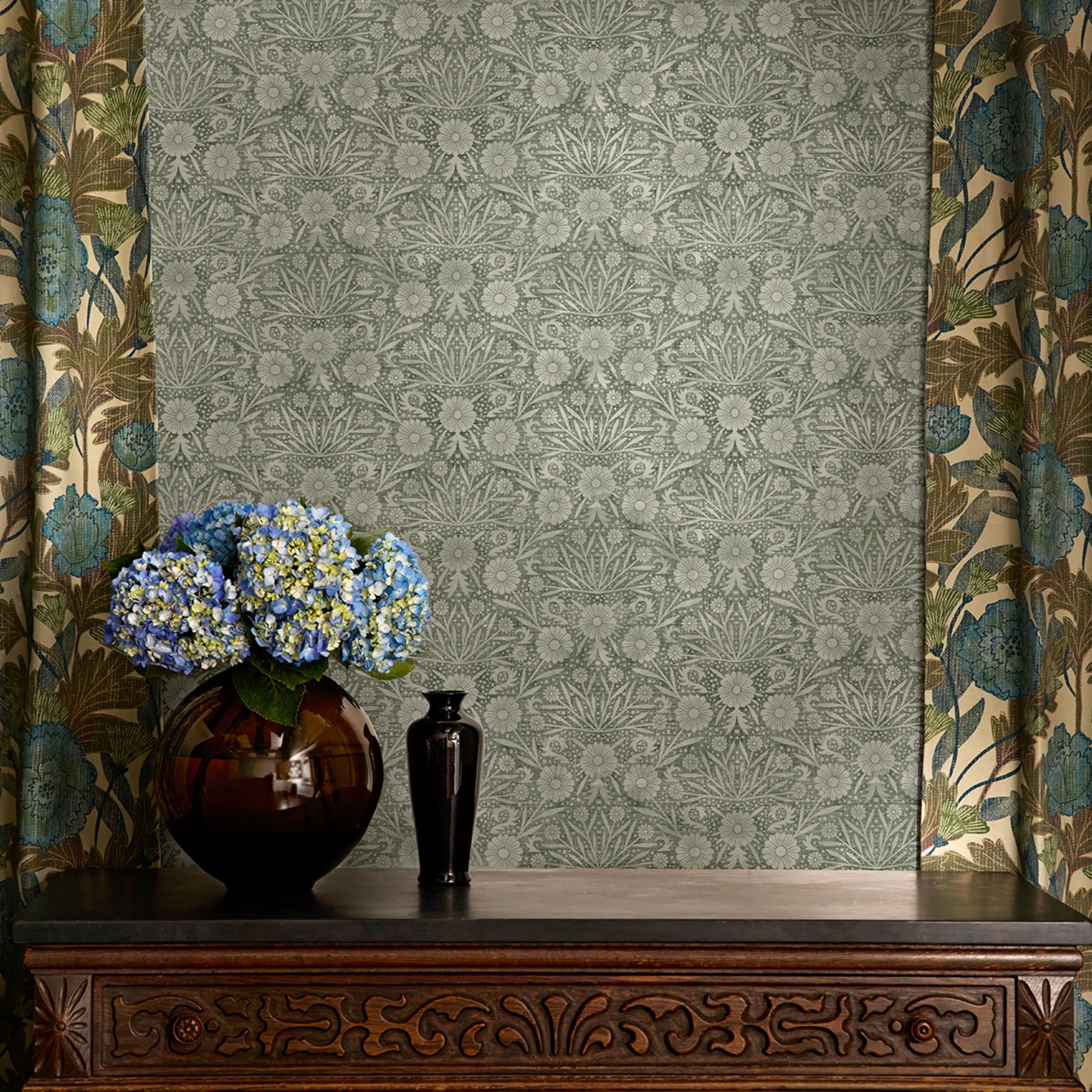Green floral damask craft revival wallpaper and botanical curtains above a vintage table.