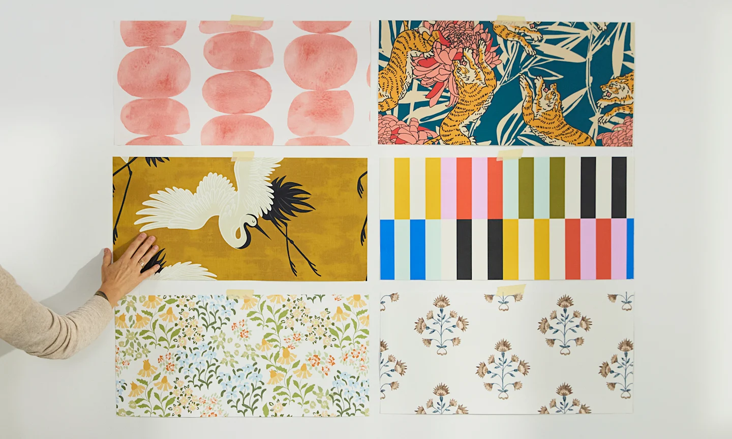 Person assessing 6 peel and stick wallpaper swatches on the wall.