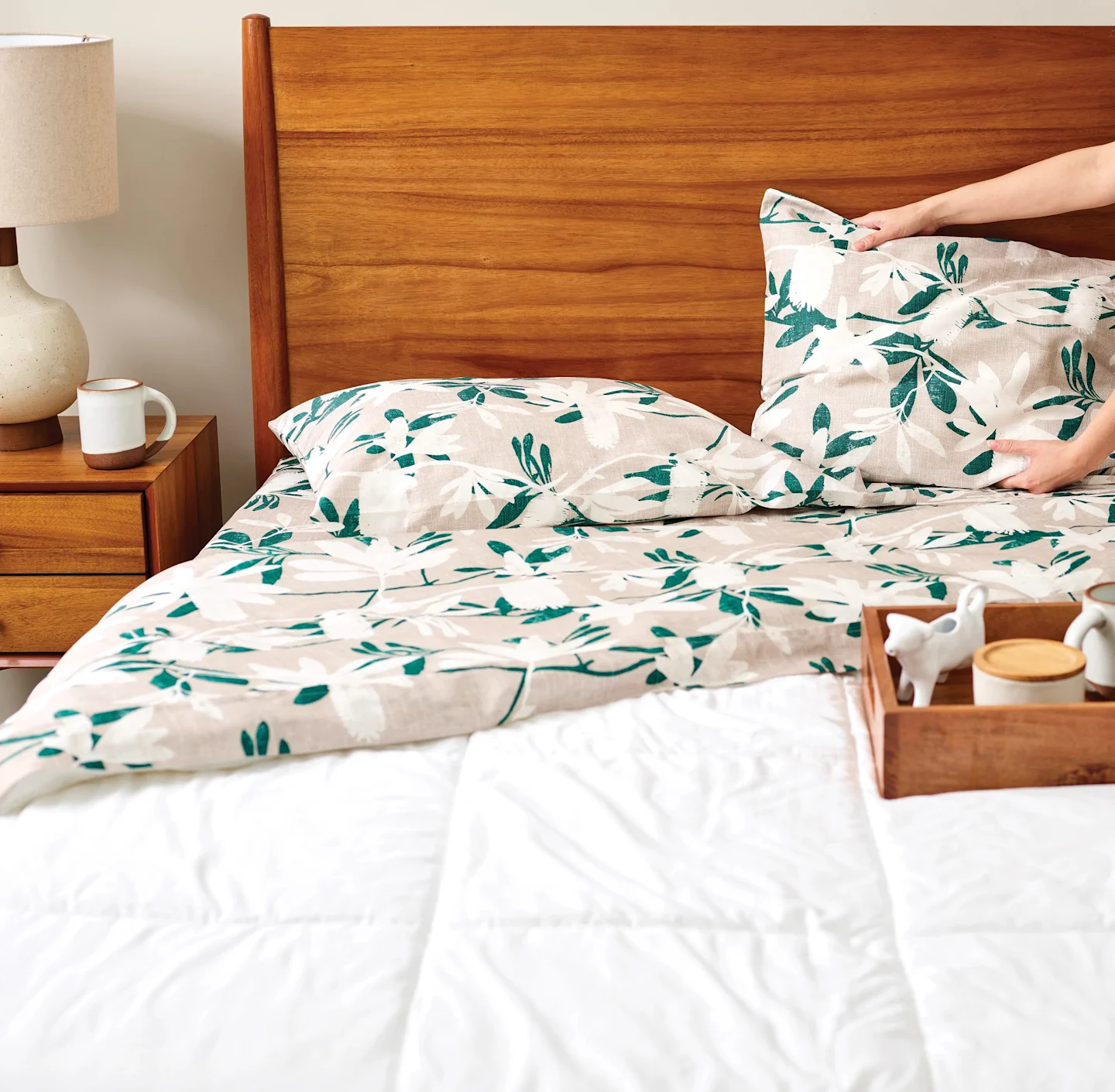 A bed with green, beige, and white watercolor floral sheets