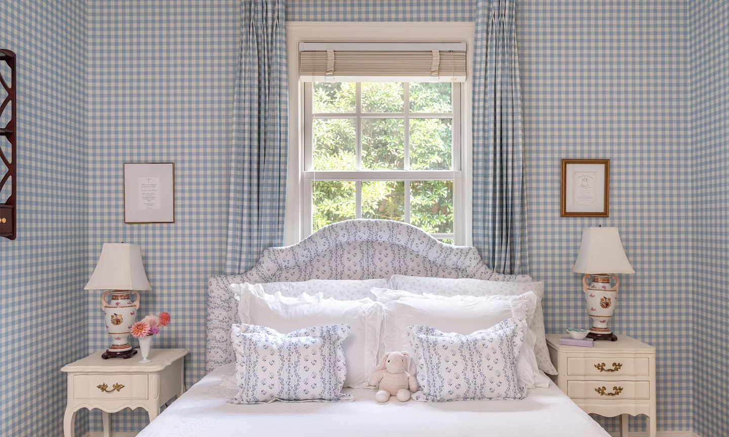 Bedroom with blue gingham wallpaper and curtains and striped floral headboard and pillows.